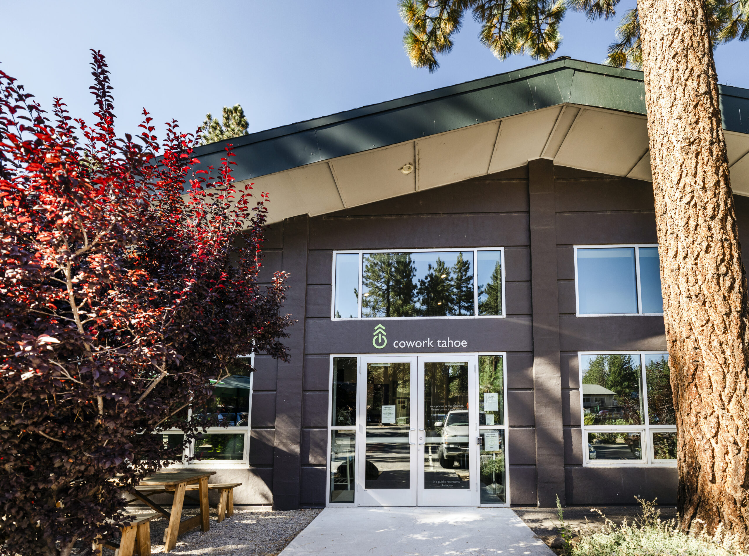 Cowork2024-003 Front Entrance of Cowork Tahoe, a brown building with glass double doors and trees to either side