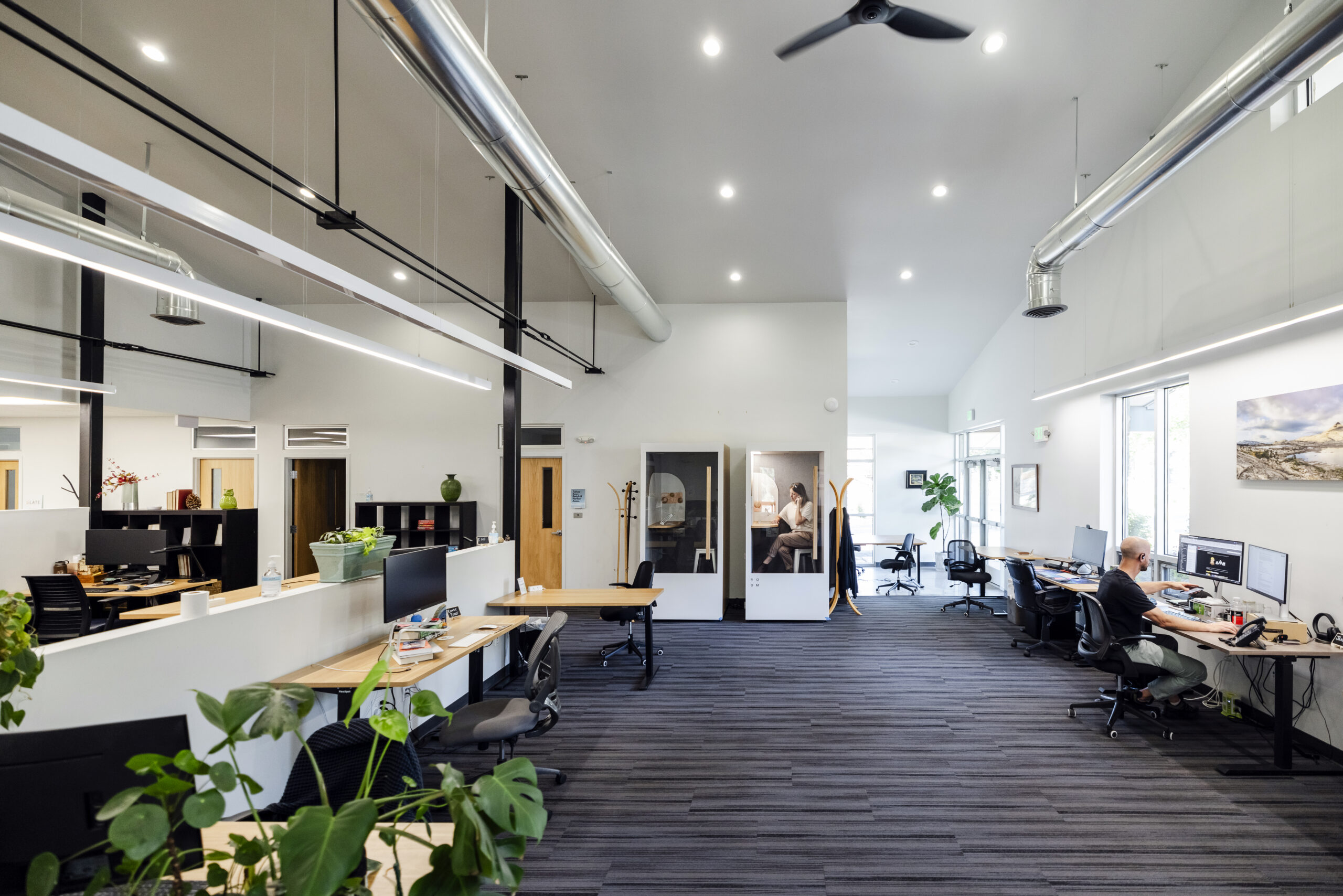 Cowork2024-074 A brightly lit open desk area with sit-stand desks and phone booths